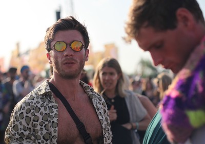 man with open shirt stood in crowd at festival wearing octagonal mirror sunglasses